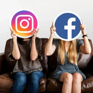 Two people on a couch holding large Instagram and Facebook logos in front of their faces.