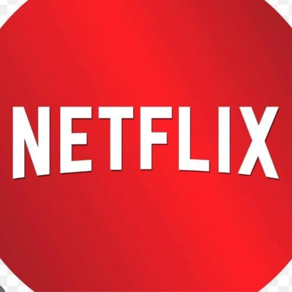 Netflix logo glowing red on a dark screen with backlit TV setup. 