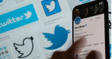 Person using a smartphone to view Elon Musk’s Twitter profile, with Twitter logos in the background.