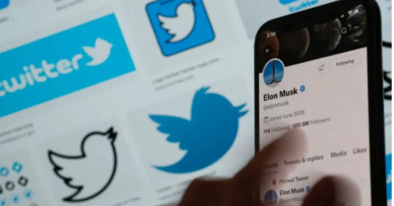 Person using a smartphone to view Elon Musk’s Twitter profile, with Twitter logos in the background.