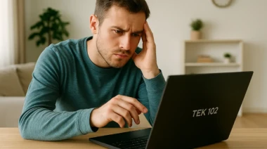 A frustrated man using a Tek 102 laptop in a bright living room.